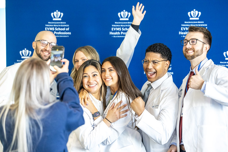 Students in white lab coats smiling as they have their photo taken