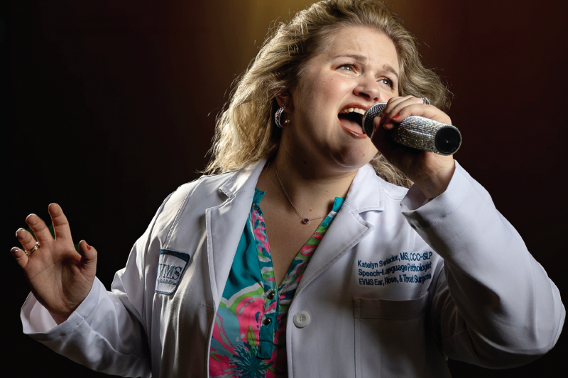 Katelyn Swiader wearing a white coat while holding and singing into a microphone