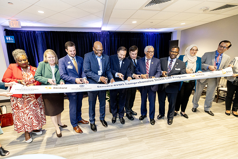 A line of various people each holding a pair of scissors cut a large ribbon.