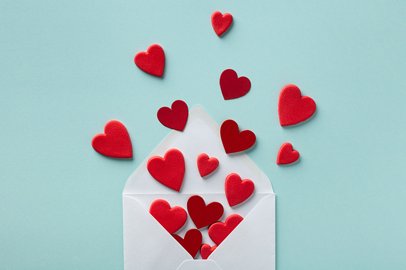 an open envelope sits on a teal blue background with red hearts spilling out of it