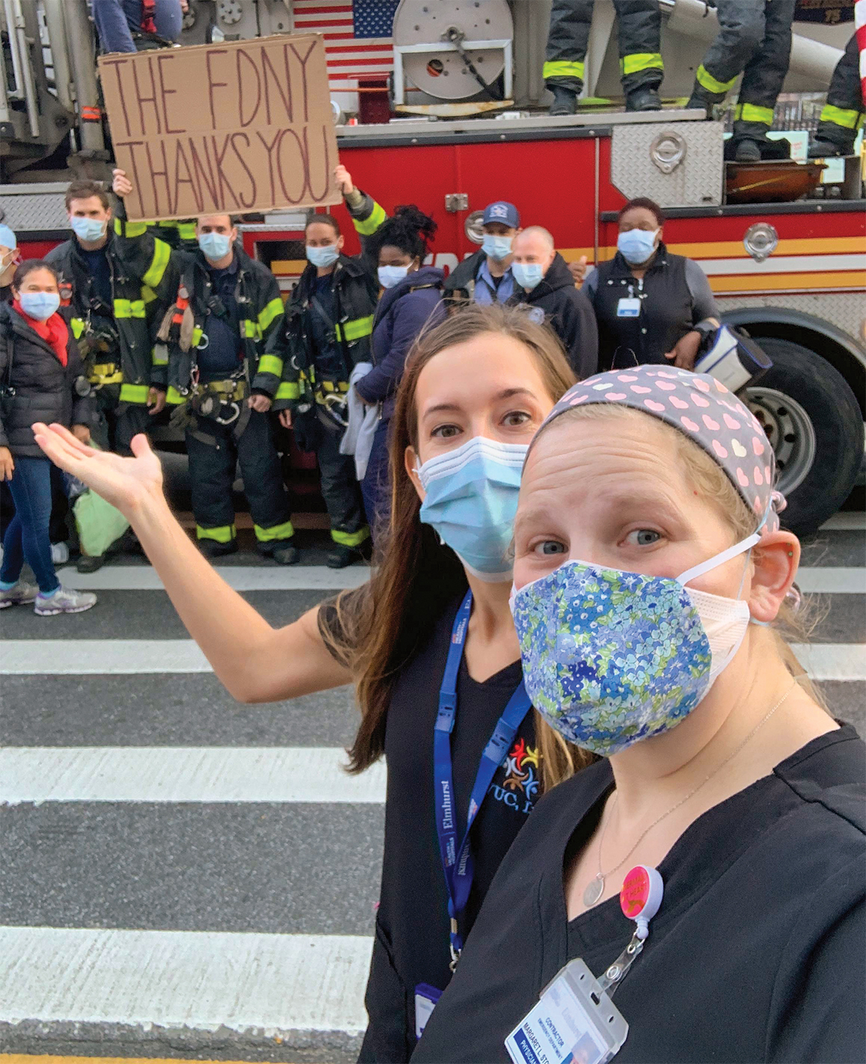 •	Margaret Stowasser poses with the New York City Fire Department and fellow health care workers on the front lines of the pandemic. The fire fighters are standing in front of a fire truck holding a sign that says 