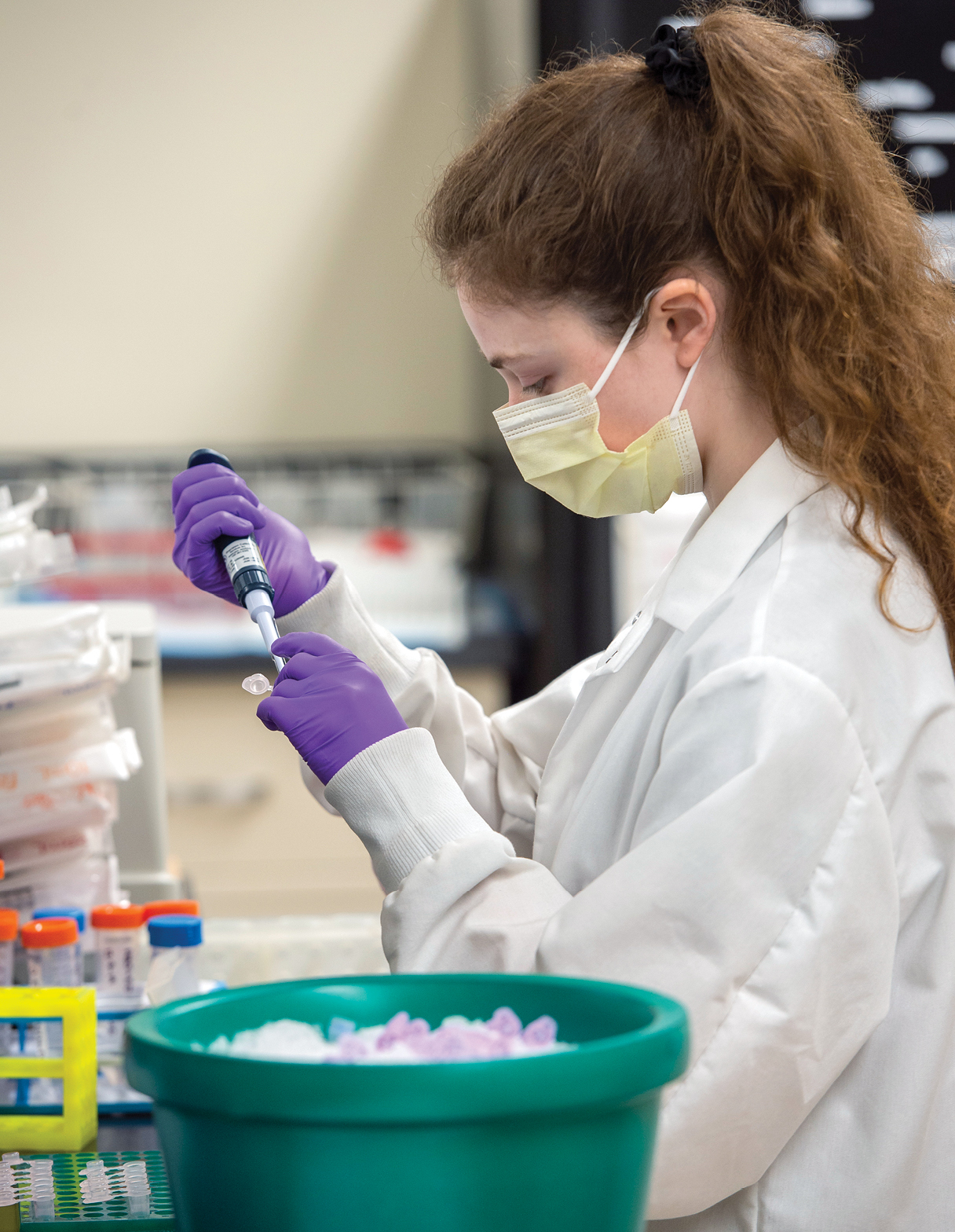 Megan Sage holds a pipette and wears a face mask and gloves while working in the lab.